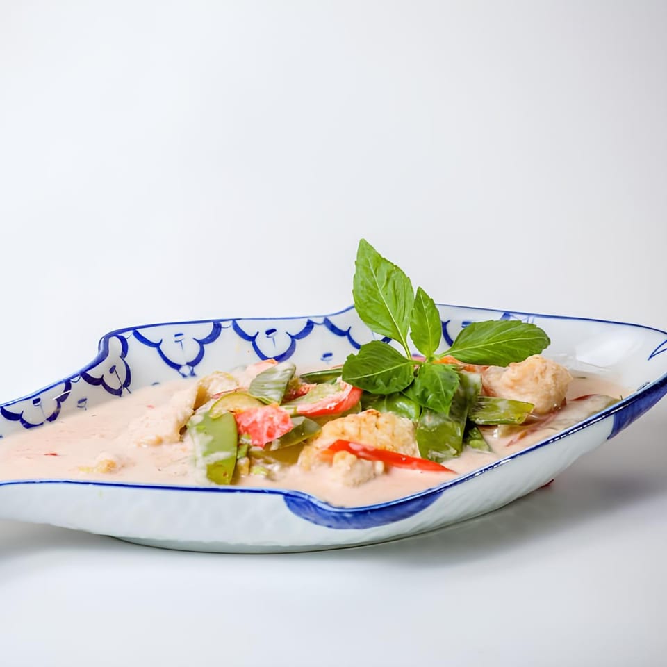 Thai red curry with chicken, green beans, red peppers, and basil in a decorative blue and white bowl.