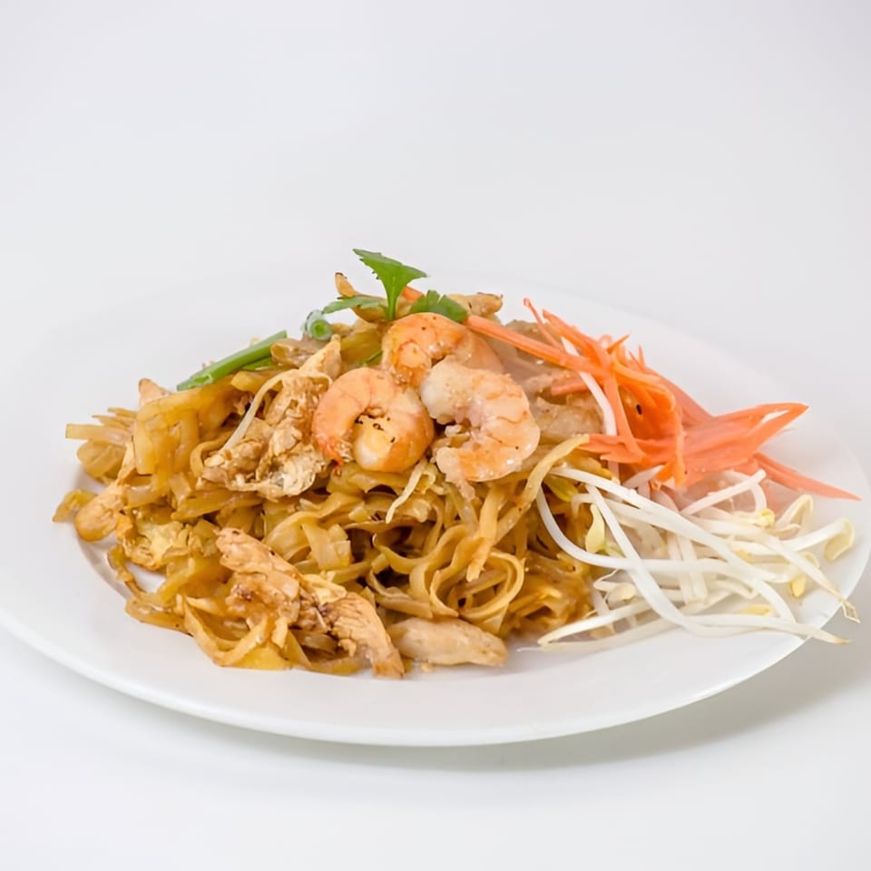 A plate of Thai Pad See Ew with chicken, shrimp, bean sprouts, and shredded carrots.