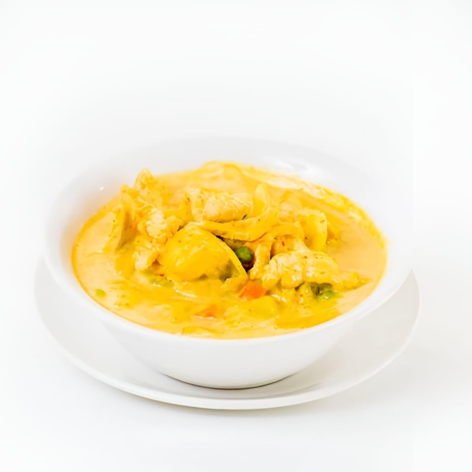 A white bowl of yellow Thai curry with chicken and vegetables on a white background.