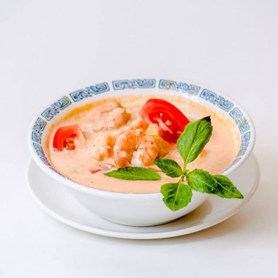 Creamy Thai soup with shrimp, tomatoes, and basil in a decorative bowl on a white background.