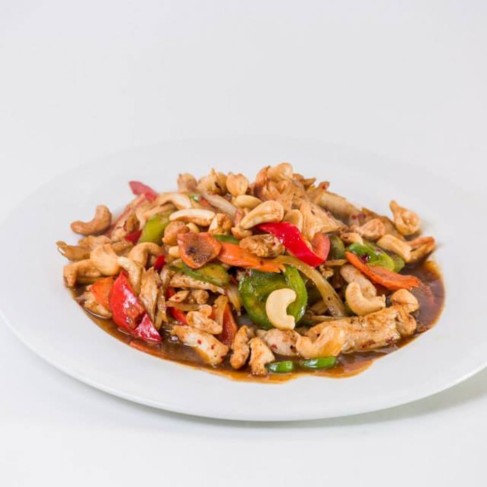 Thai cashew chicken stir-fry with red and green bell peppers, onions, and carrots on a white plate.
